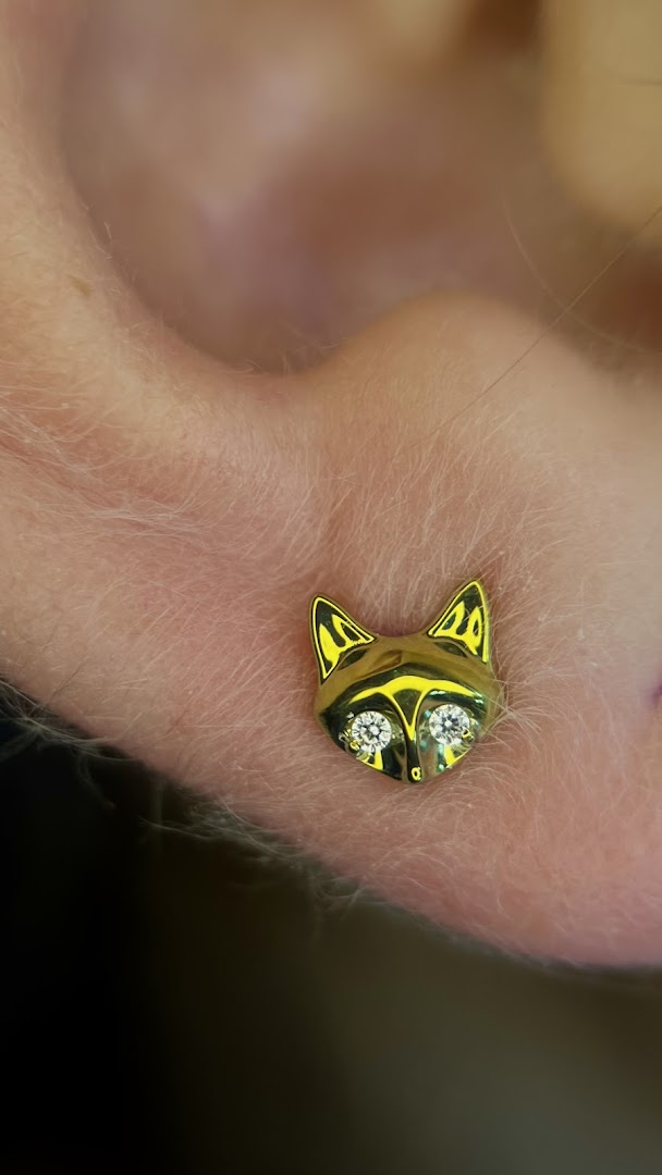 A close-up of a gold fox-shaped piercing with diamond eyes on an ear.