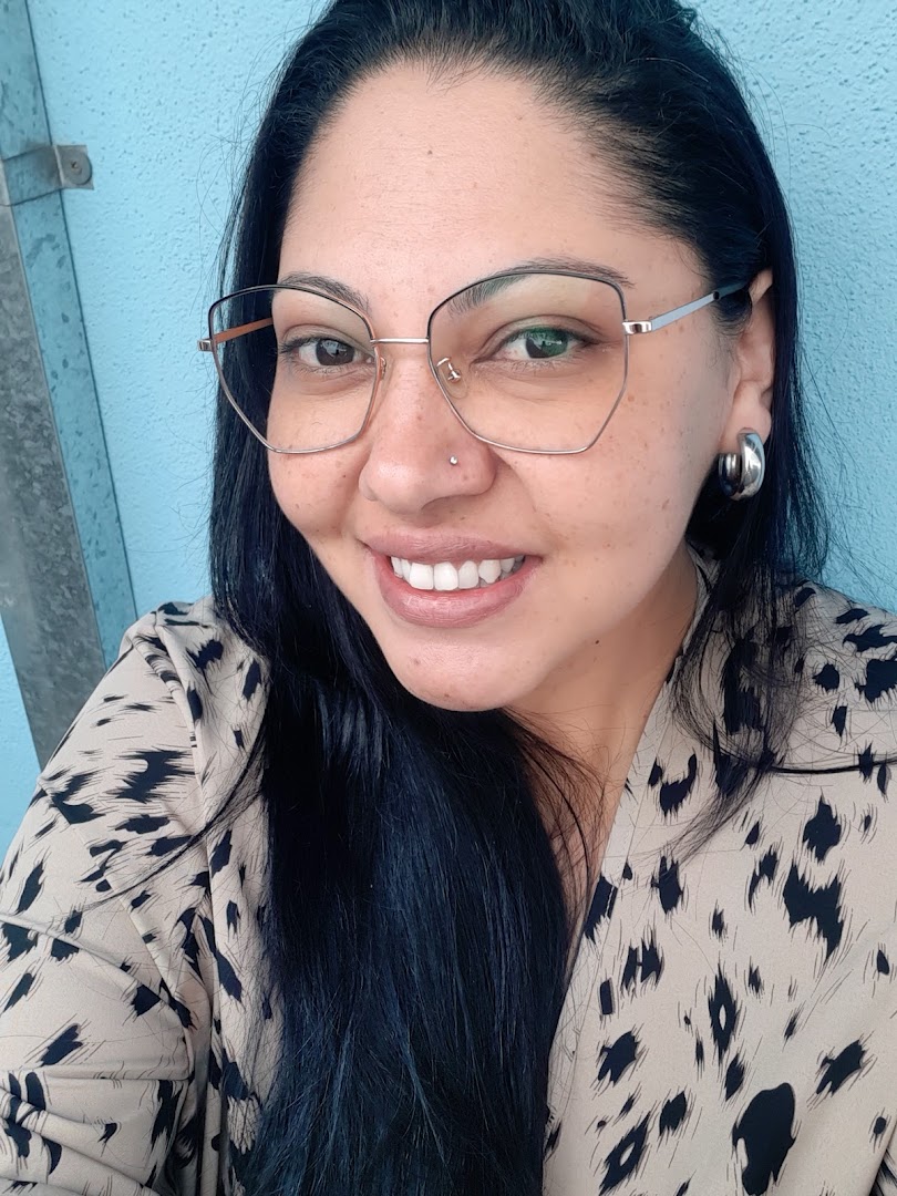 A woman with dark hair, glasses, and a nose piercing smiles at the camera.