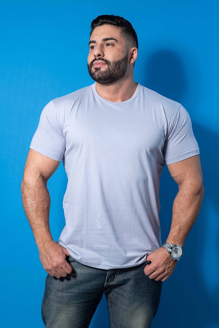 A man with a beard wearing a light blue t-shirt and jeans against a blue background.