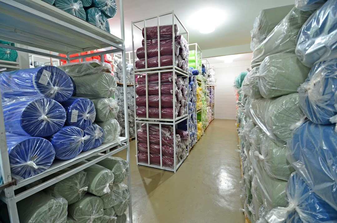 A warehouse aisle filled with shelves of rolled fabrics in various colors, neatly packaged.