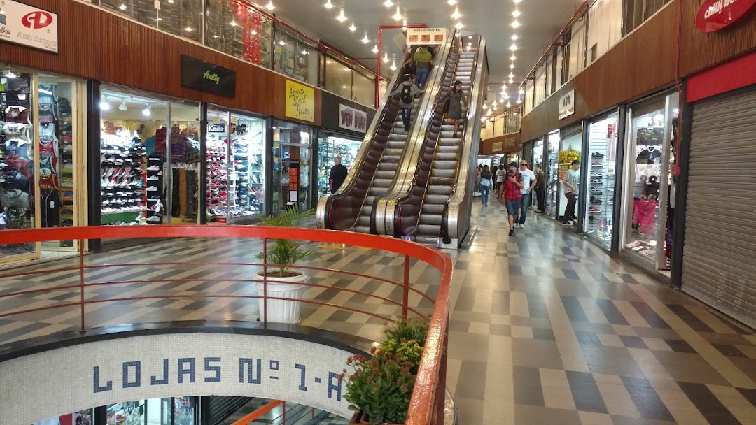 Interior view of a shopping mall with escalators and various retail shops displaying merchandise.