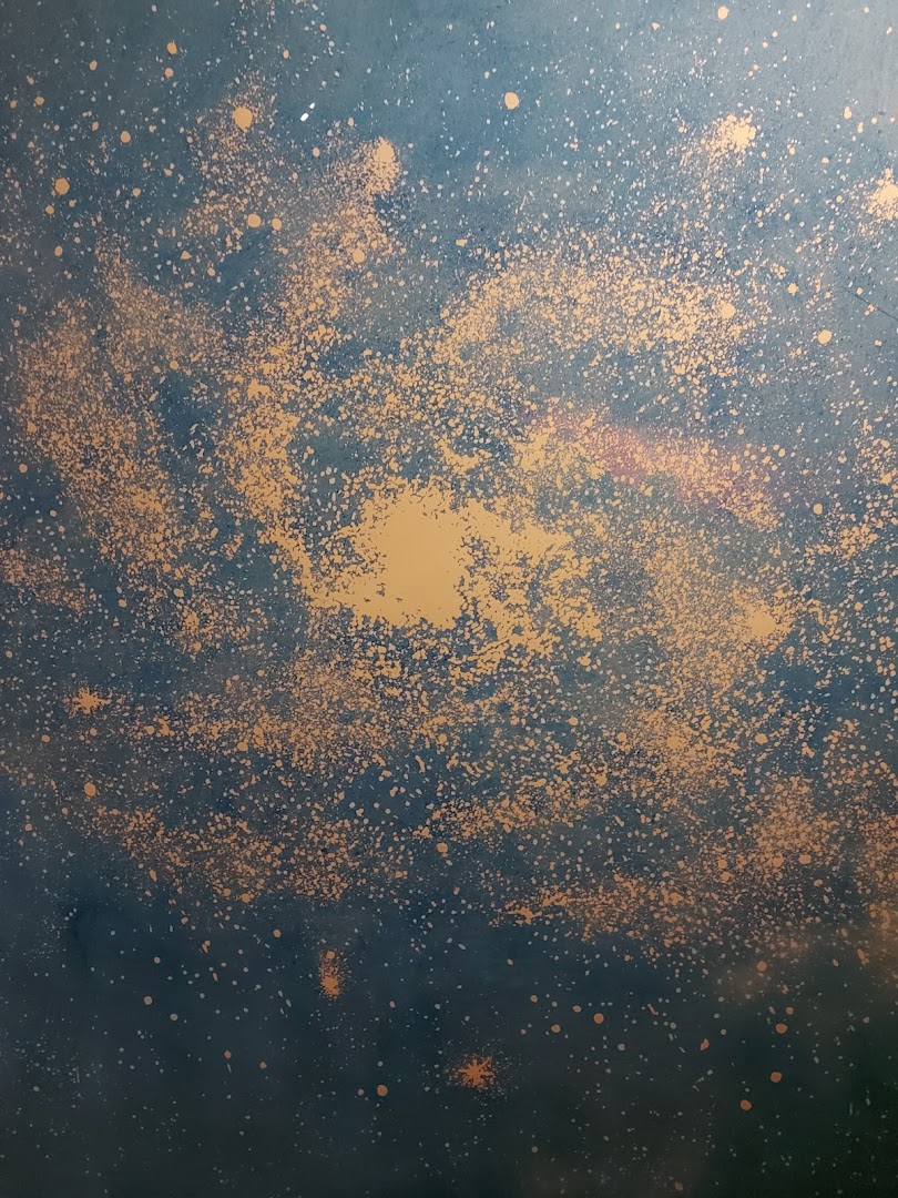 A dark blue background with a splatter of gold and white paint resembling a galaxy.