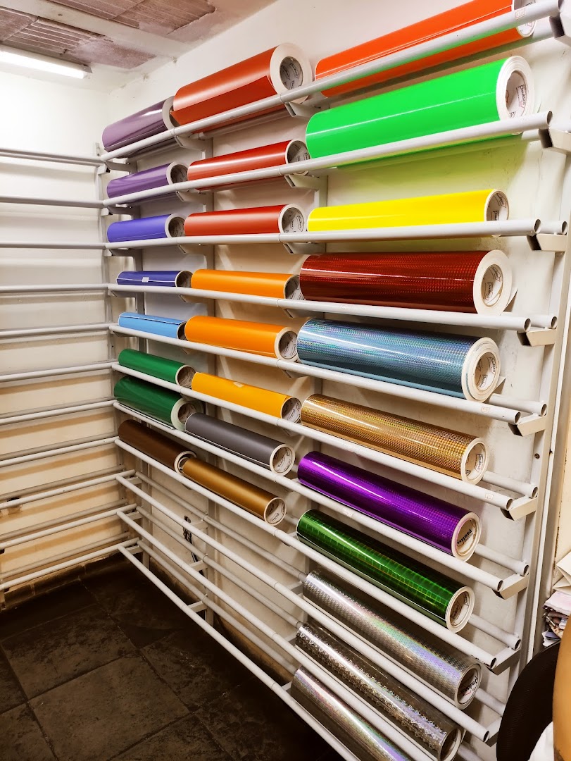A wall rack filled with rolls of colorful vinyl and holographic material.
