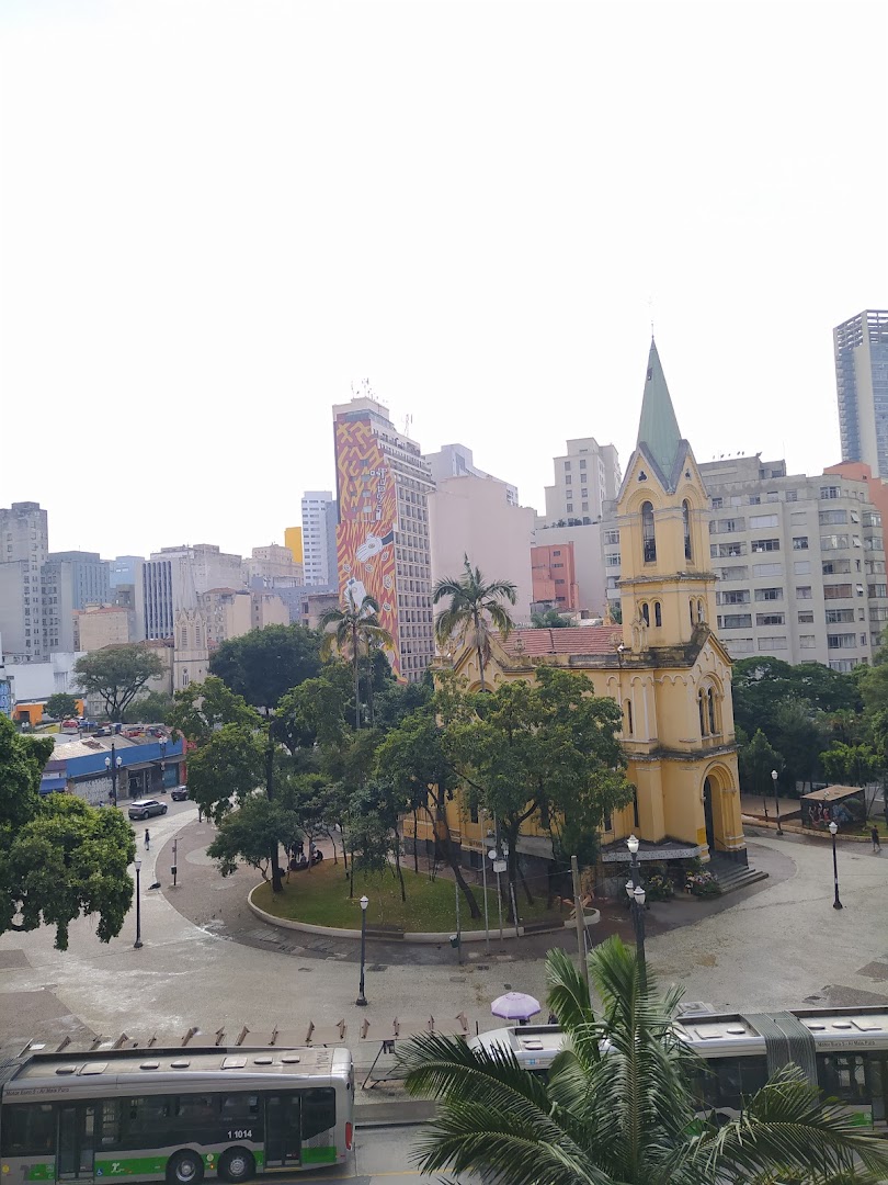 A city square with a yellow church, trees, buildings, and buses.