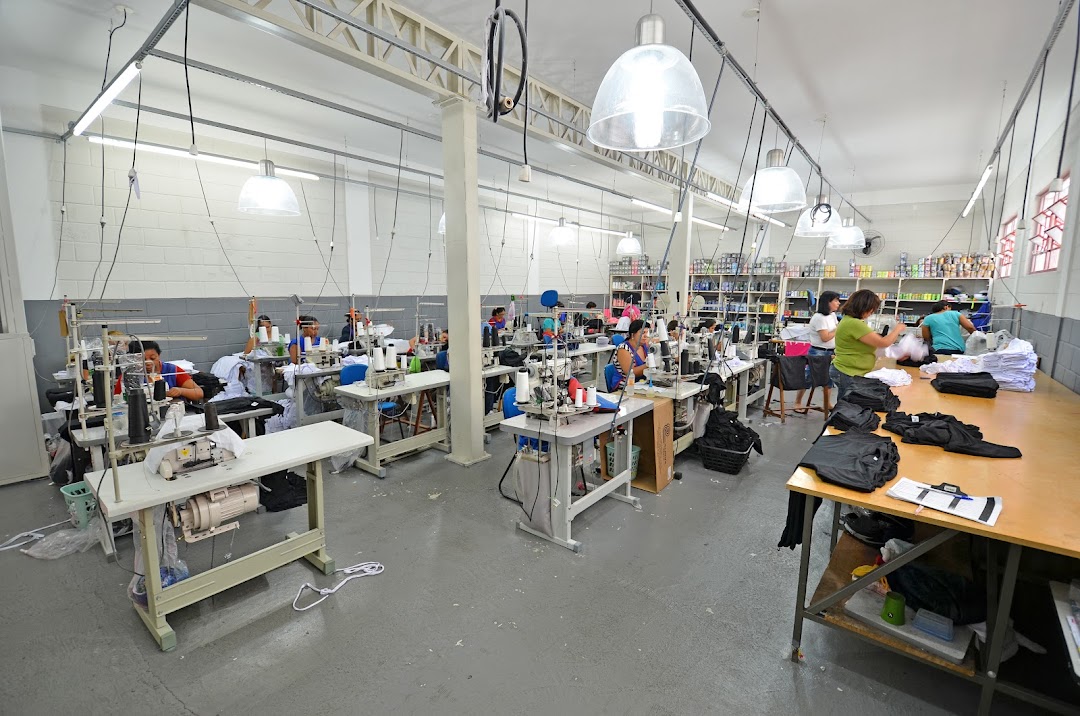 A busy garment factory with workers sewing at multiple stations and fabric being prepared.