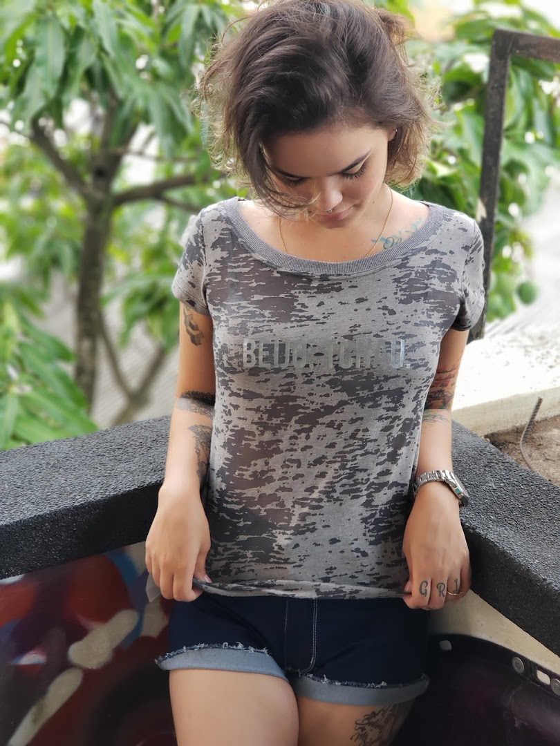A young woman with tattoos wears a distressed grey t-shirt and denim shorts.