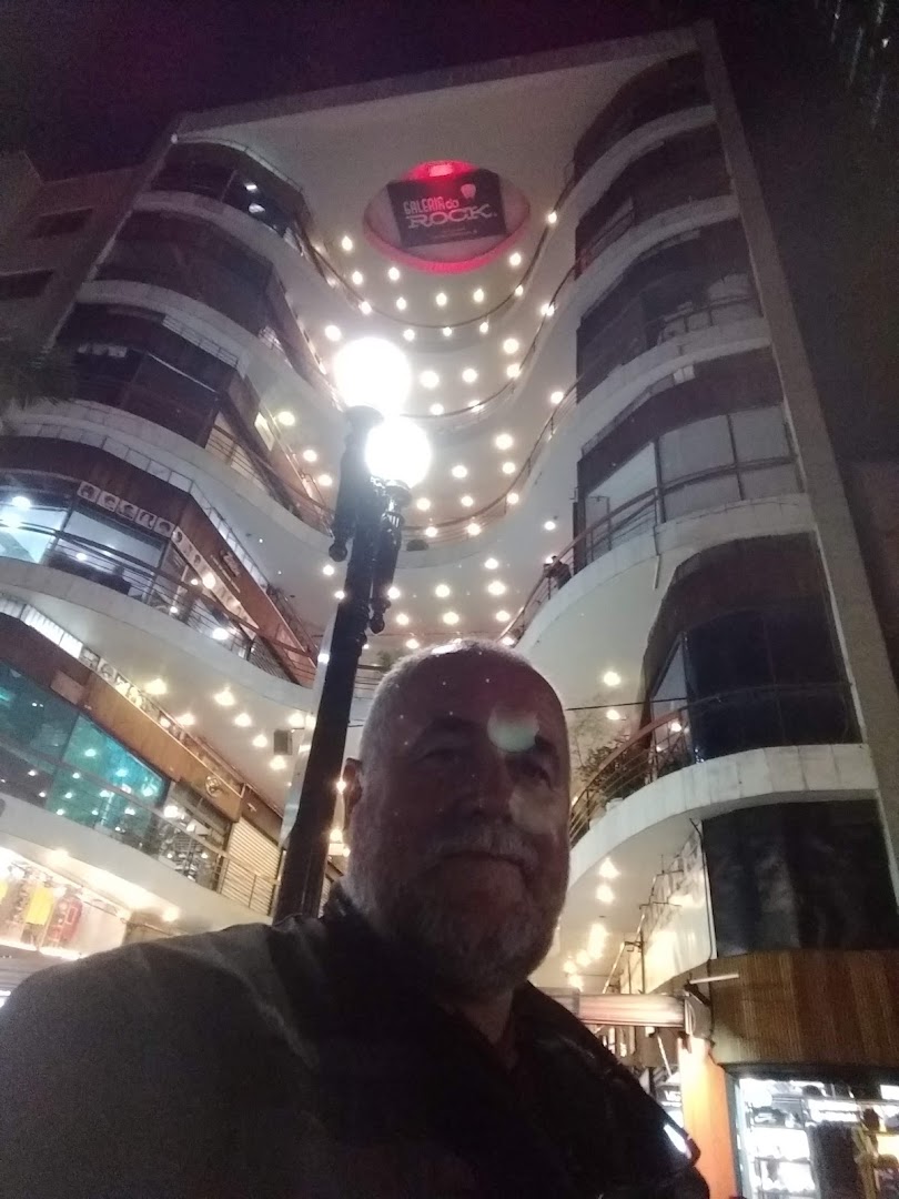 A man stands in front of a multi-story building with many lights and shops.