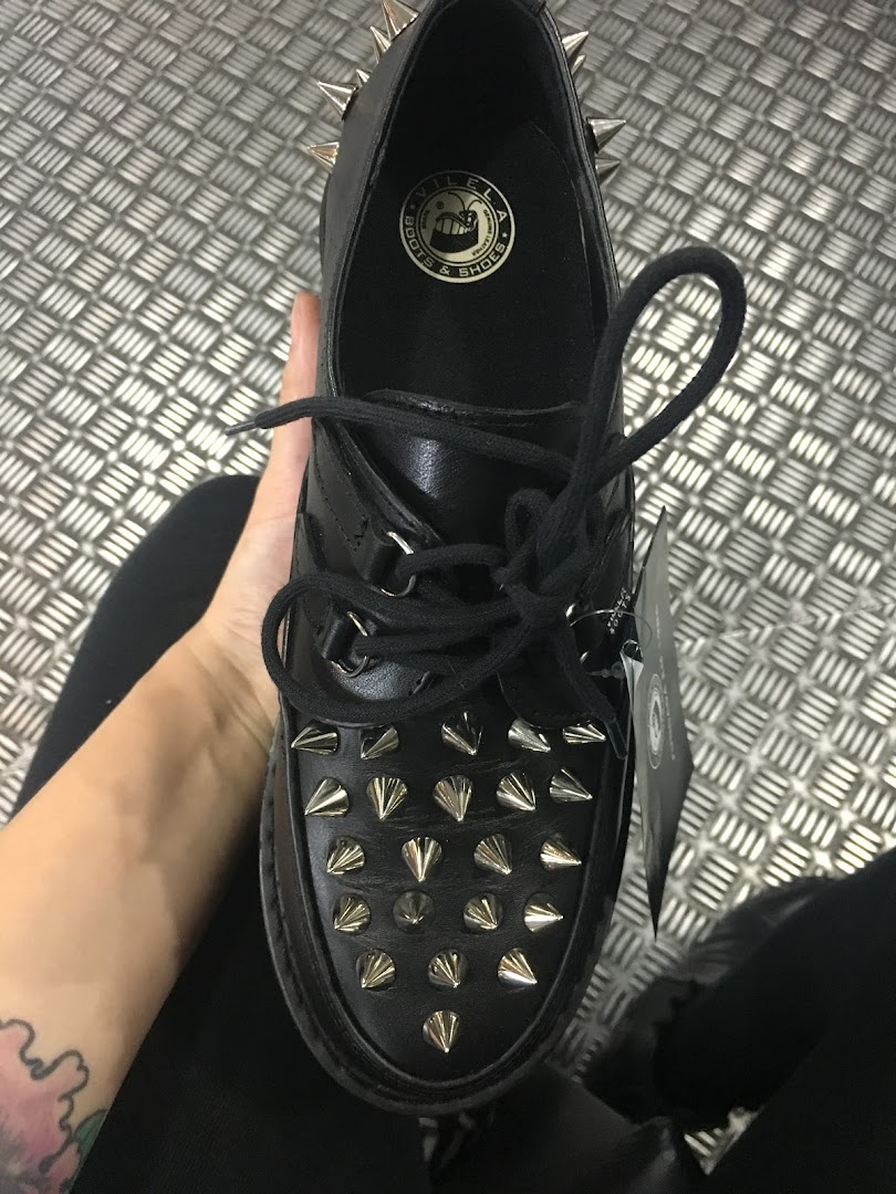 A person holds a black leather shoe with spikes and laces from Vilela Boots.