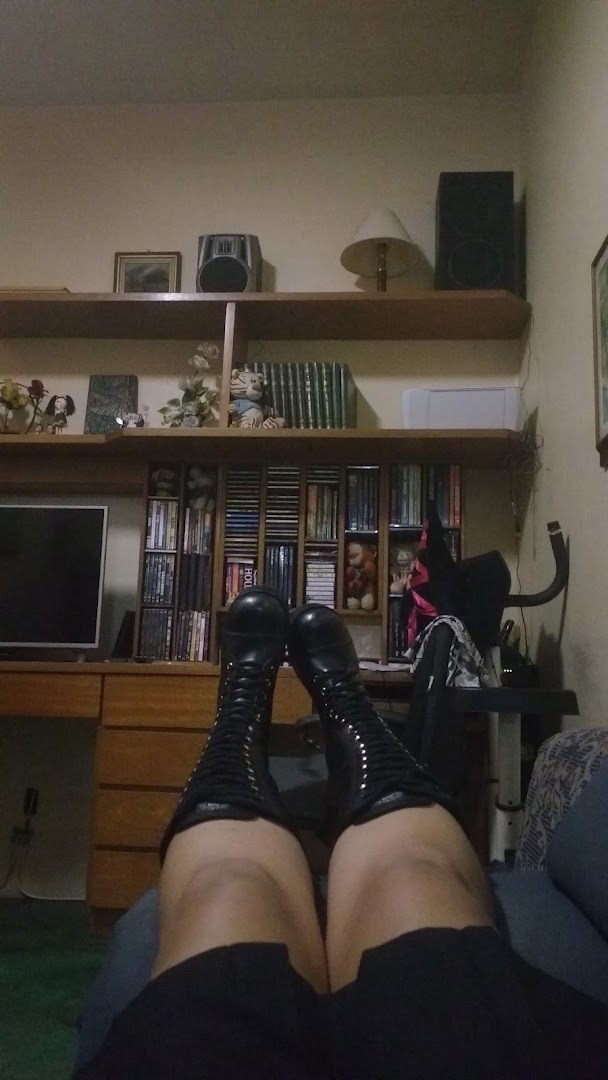A person wearing tall black lace-up boots and black shorts, relaxing indoors.