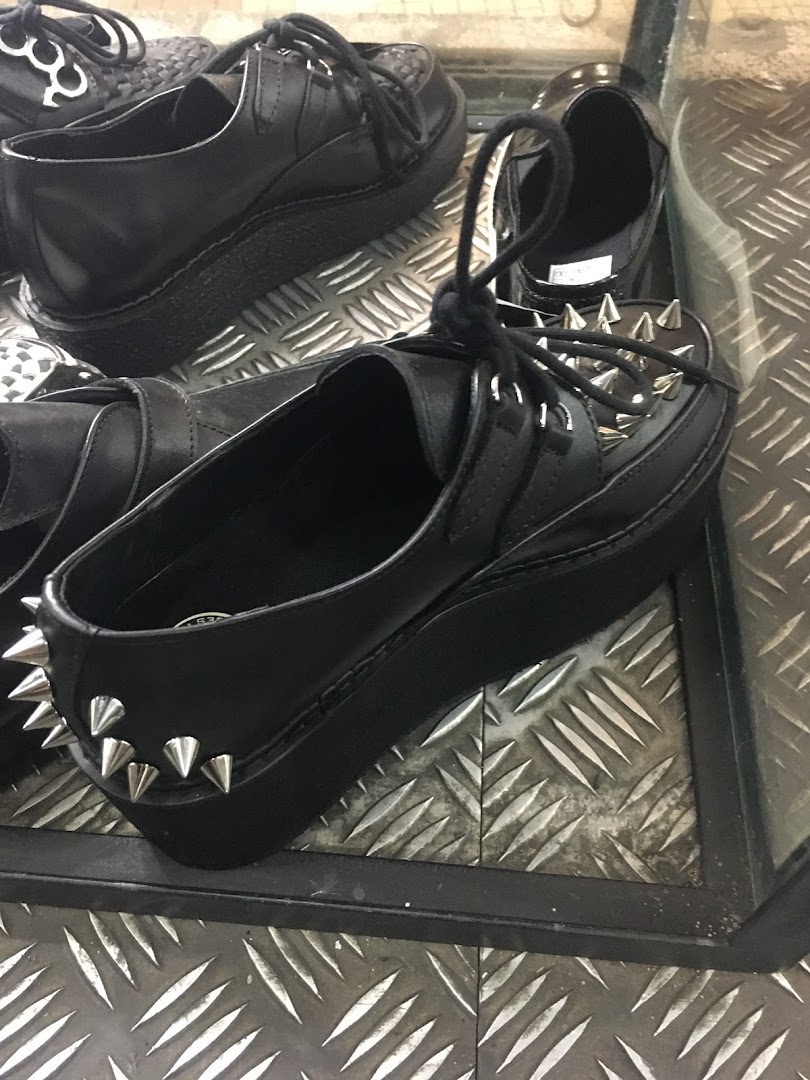 Close-up of black platform shoes with spikes and laces, displayed in a shop.