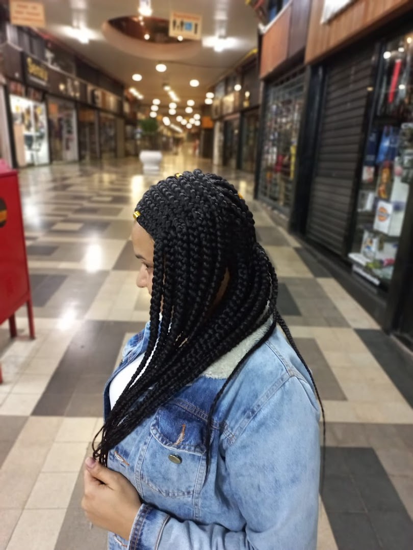 A woman with long, braided hair stands in a shopping mall corridor.