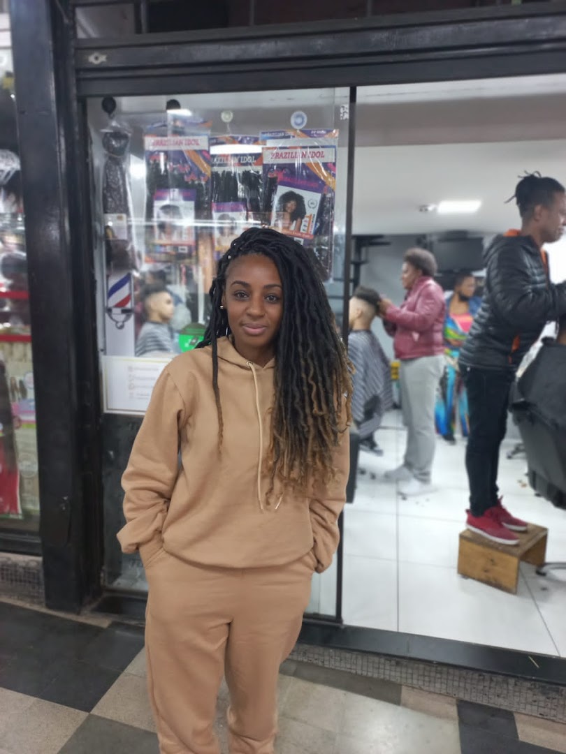 A woman with dreadlocks stands in front of a hair salon displaying hair products.