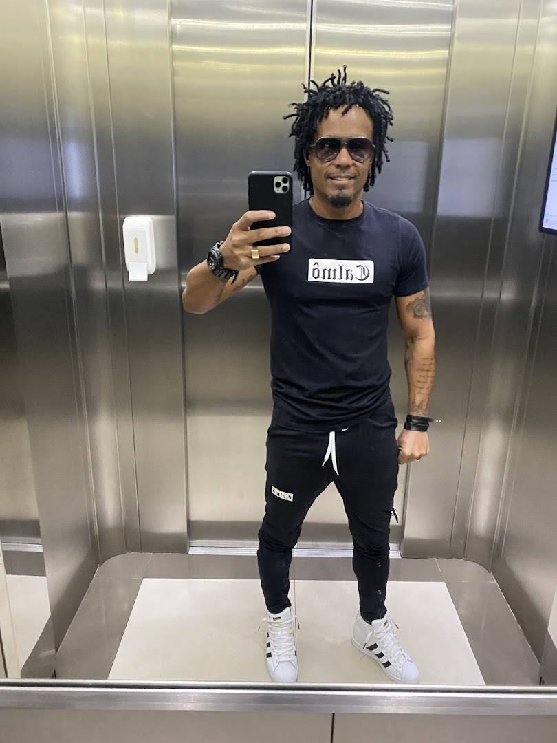 A man in a black t-shirt and pants takes a selfie in an elevator.
