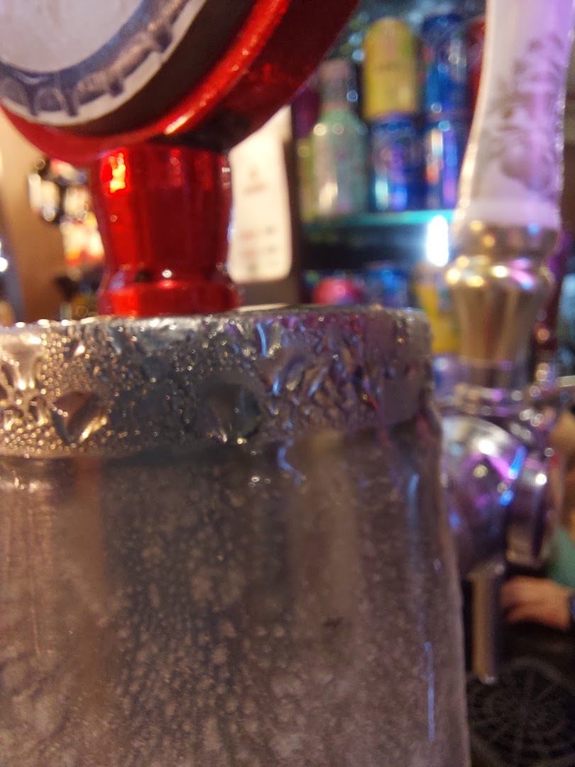 Close-up of a frosty glass with a red tap and bottles in the background.